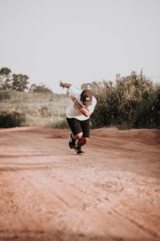 A young man wearing casual attire runs on a dirt path surrounded by nature on a sunny day.